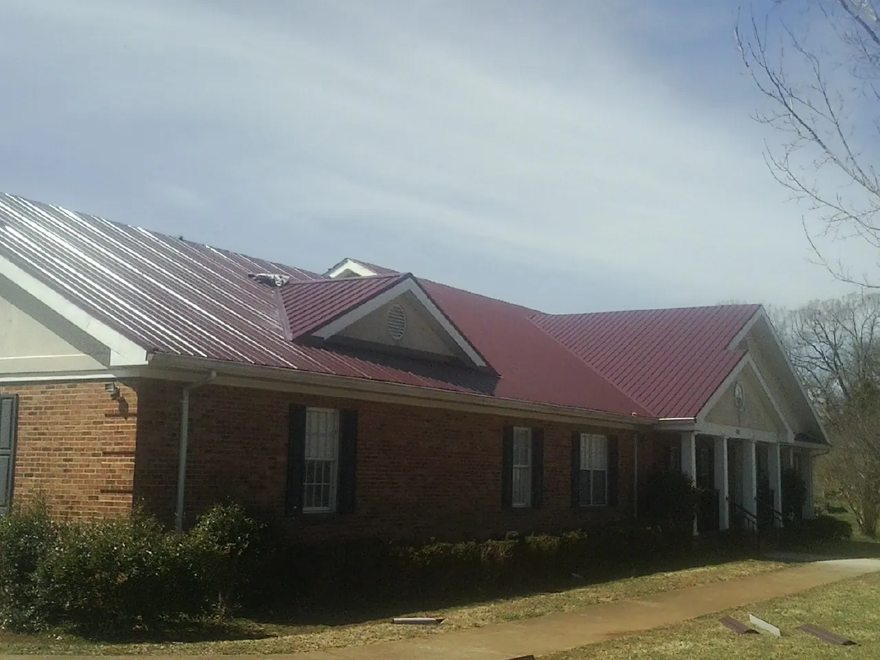 Red metal roof with gabled entries on a long brick building, from a Hail Damage Roof Repair job in Wallingford