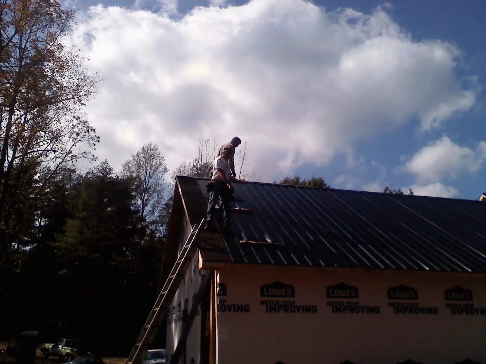 Roofer fastening dark metal panels high against a cloudy sky, from a Roof Inspection job in Wallingford
