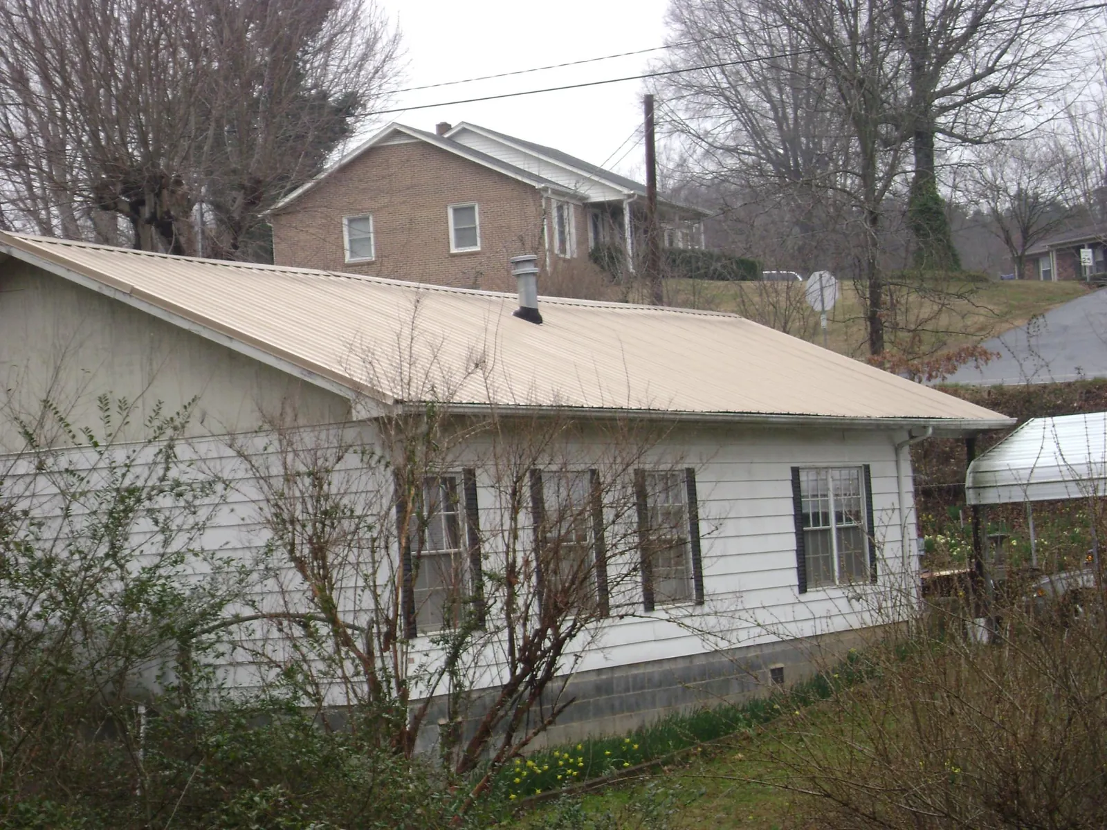 Tan metal roof on a white sided house set into a hillside — Commercial Roofing by Roofing Brothers in Wallingford